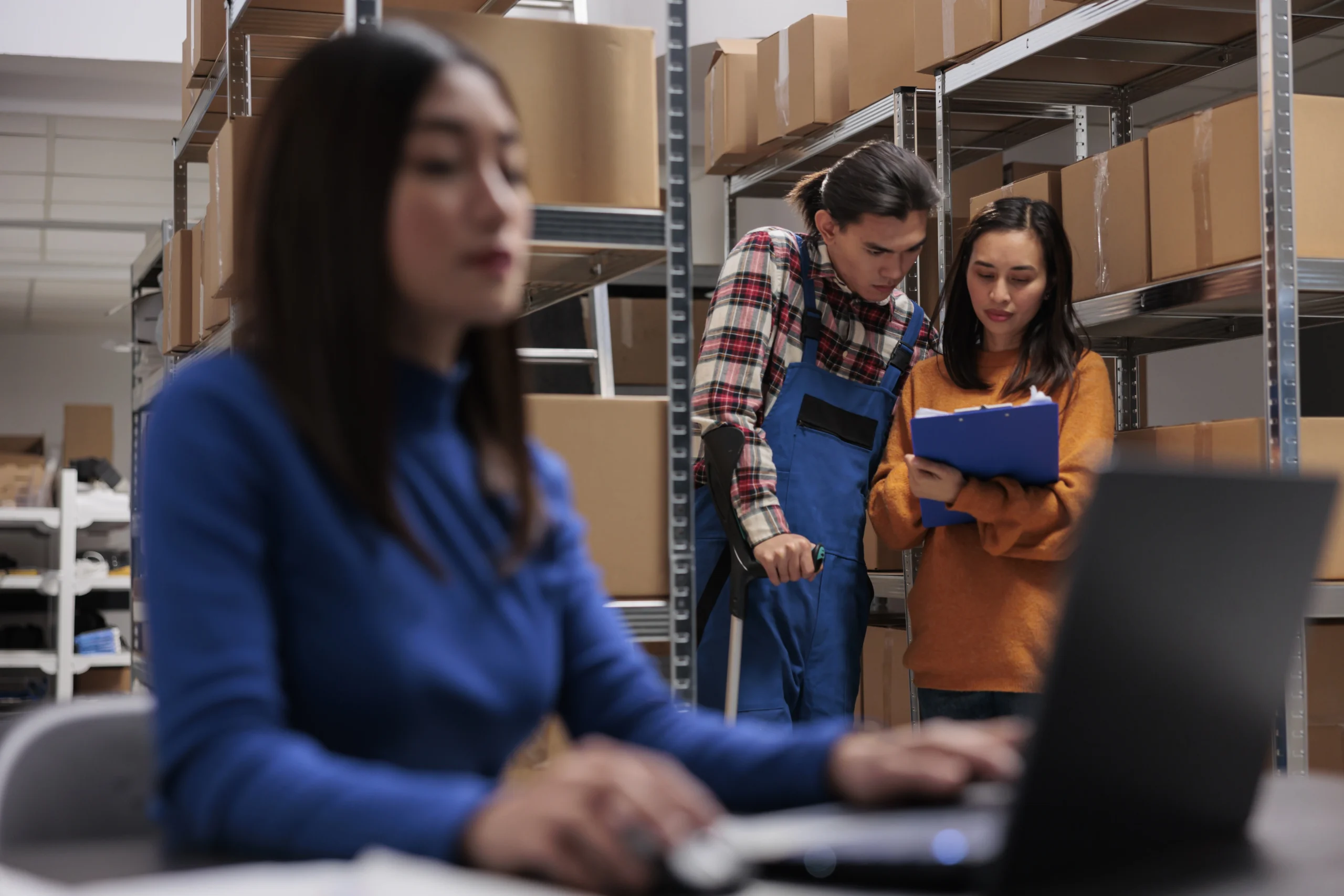 storehouse-managers-holding-clipboard-analyzing-distribution-report-retail-storage-room-asian-delivery-operator-using-crutches-working-warehouse-with-logistics-operator